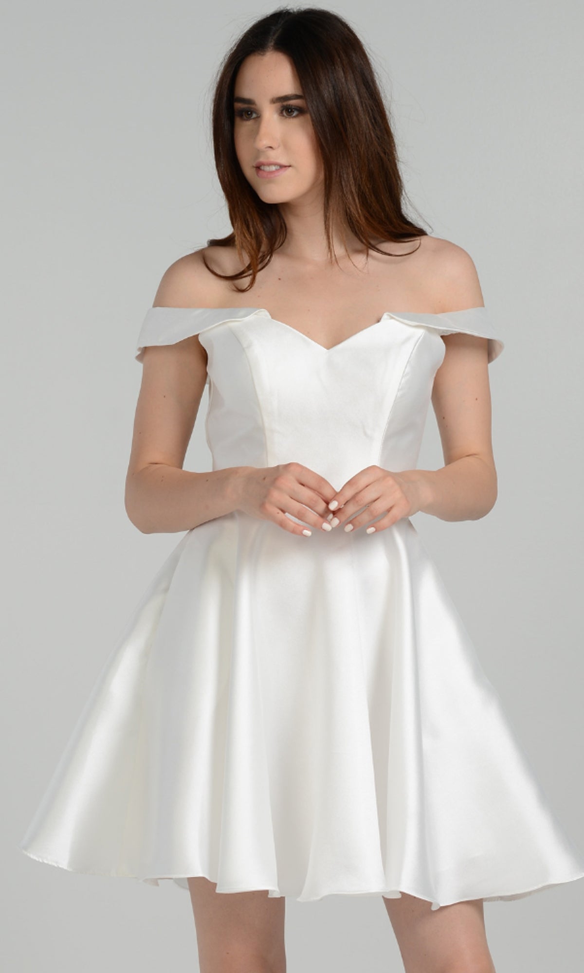 A woman stands against a plain light gray background wearing the Off-Shoulder Short Mikado Homecoming Dress 7948, a white knee-length dress with an off-the-shoulder design.